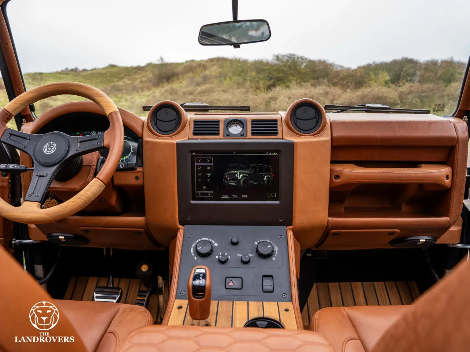 The central infotainment touchscreen and physical controls in Alcide’s tan dashboard, with the digital cluster visible behind the steering wheel.